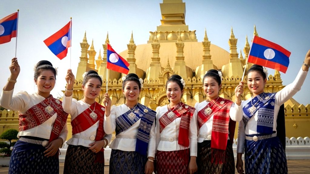 สาวลาวในชุดประจำชาติ ถือธงชาติลาว หน้าพระธาตุหลวงเวียงจันทน์